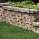 A stone retaining wall stands prominently, with a lush garden flourishing in the background, showcasing Laytonscape's design.