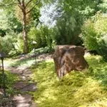 A garden scene showcasing a prominent stone, encircled by trees and diverse plants, created by Laytonscape